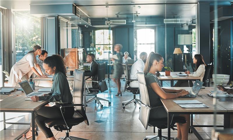 Modern open-plan office with diverse team collaborating and working on laptops, reflecting AI-enabled workflows and a digitally transformed operating model