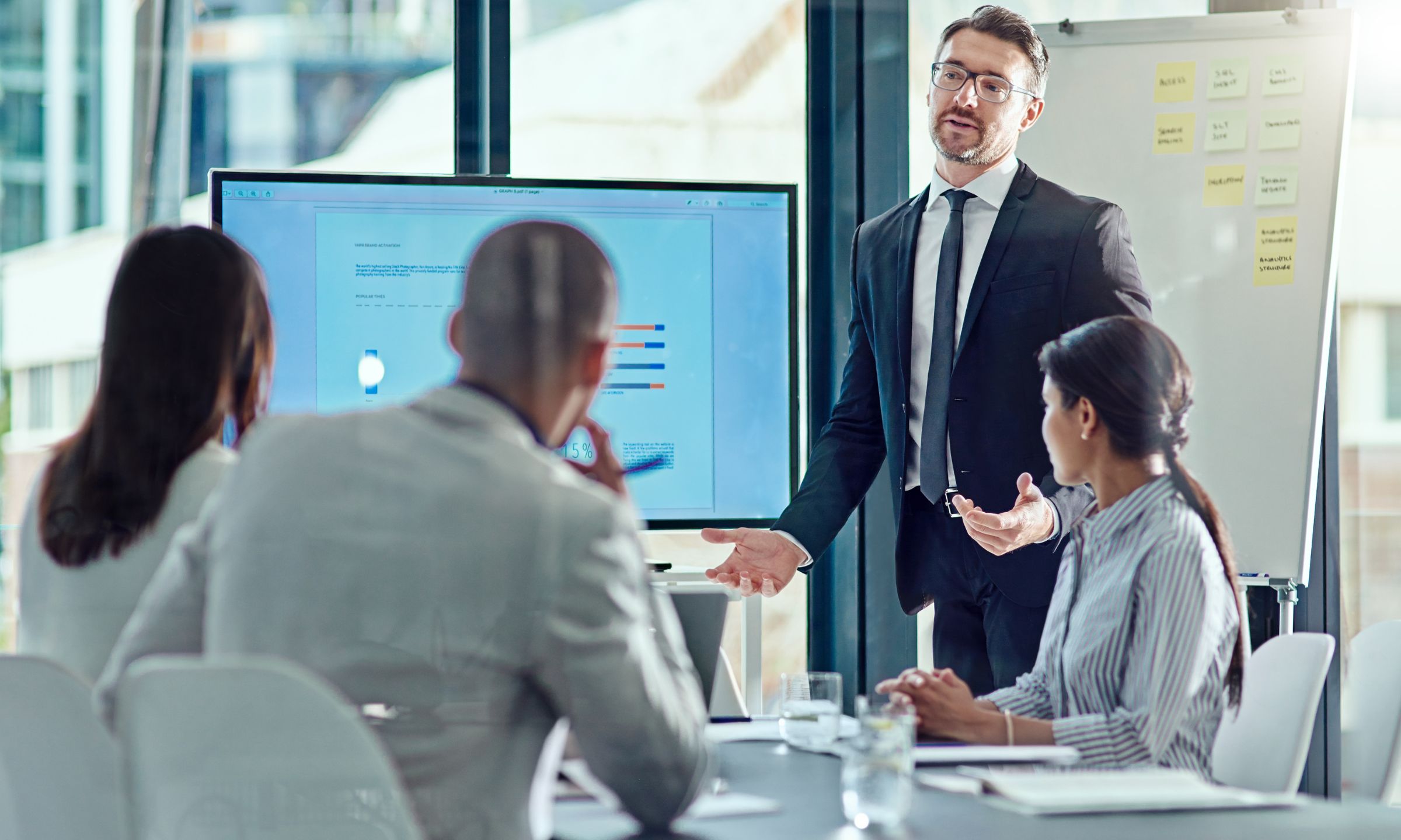 Business professional presenting data on a screen to colleagues during a meeting, discussing performance insights and strategy
