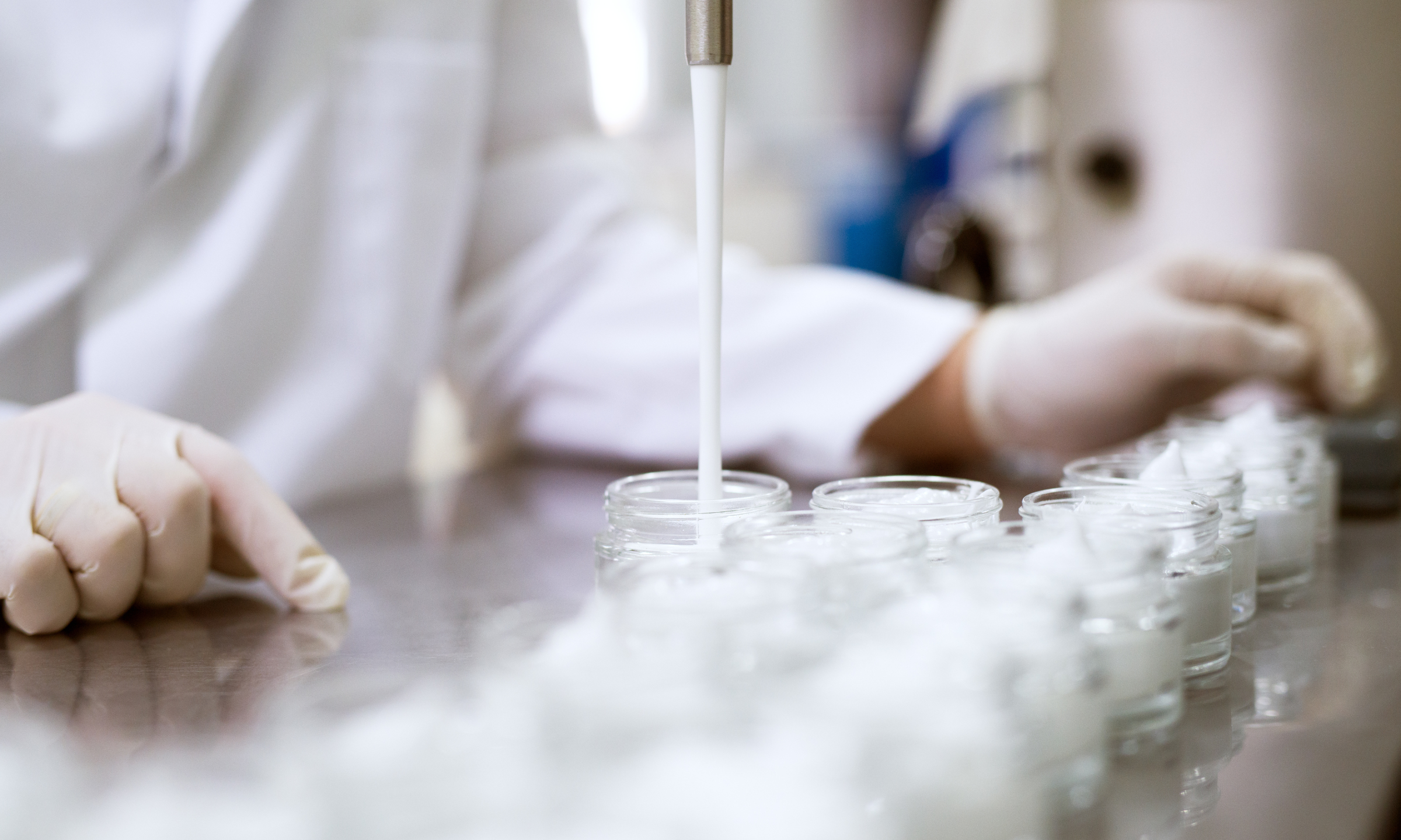 Scientist filling cosmetic cream jars in a laboratory production line.