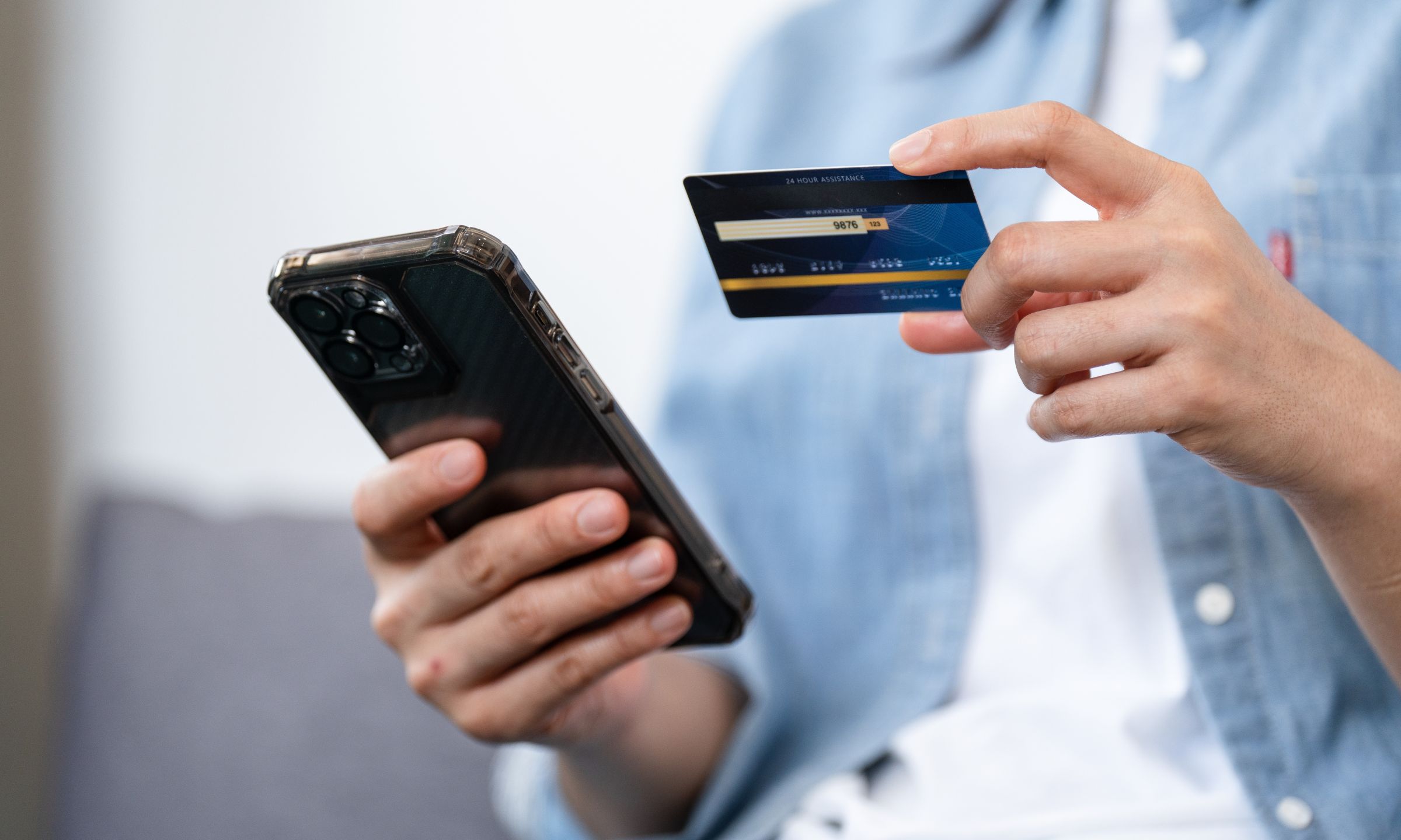 Person holding a credit card while using a smartphone for online payment.